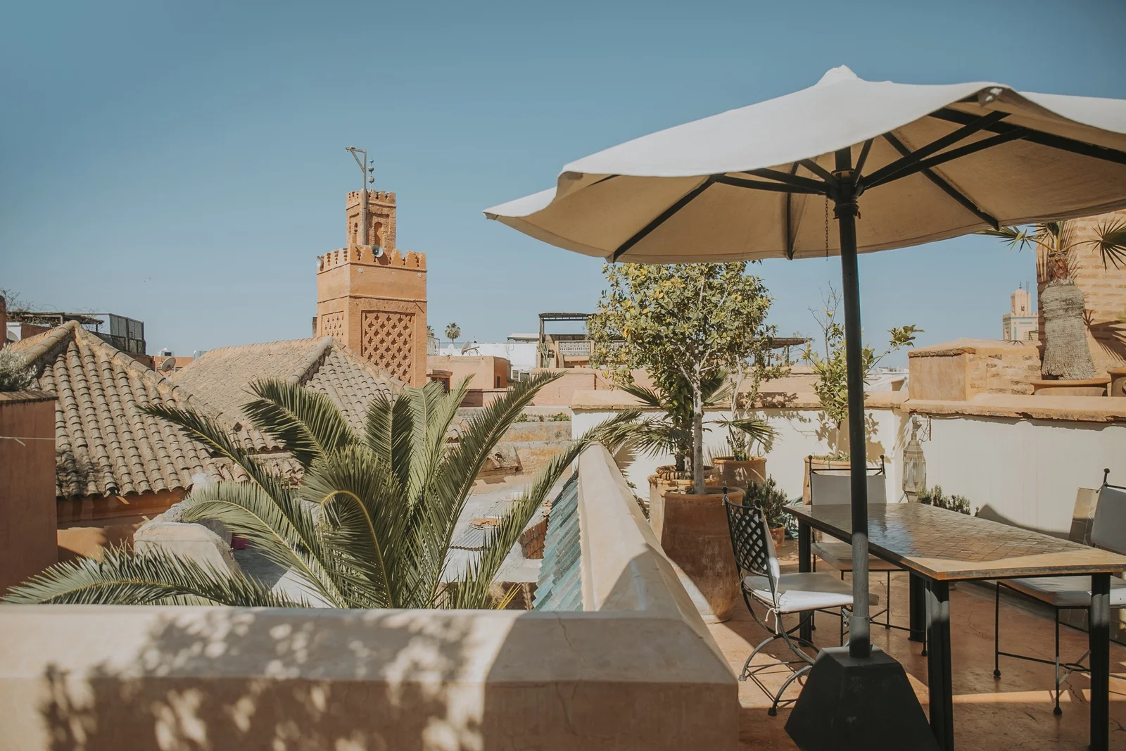 The rooftop terrace of Dar Zelda — parasol, potted citrus and the minaret of Kaât Bennahid