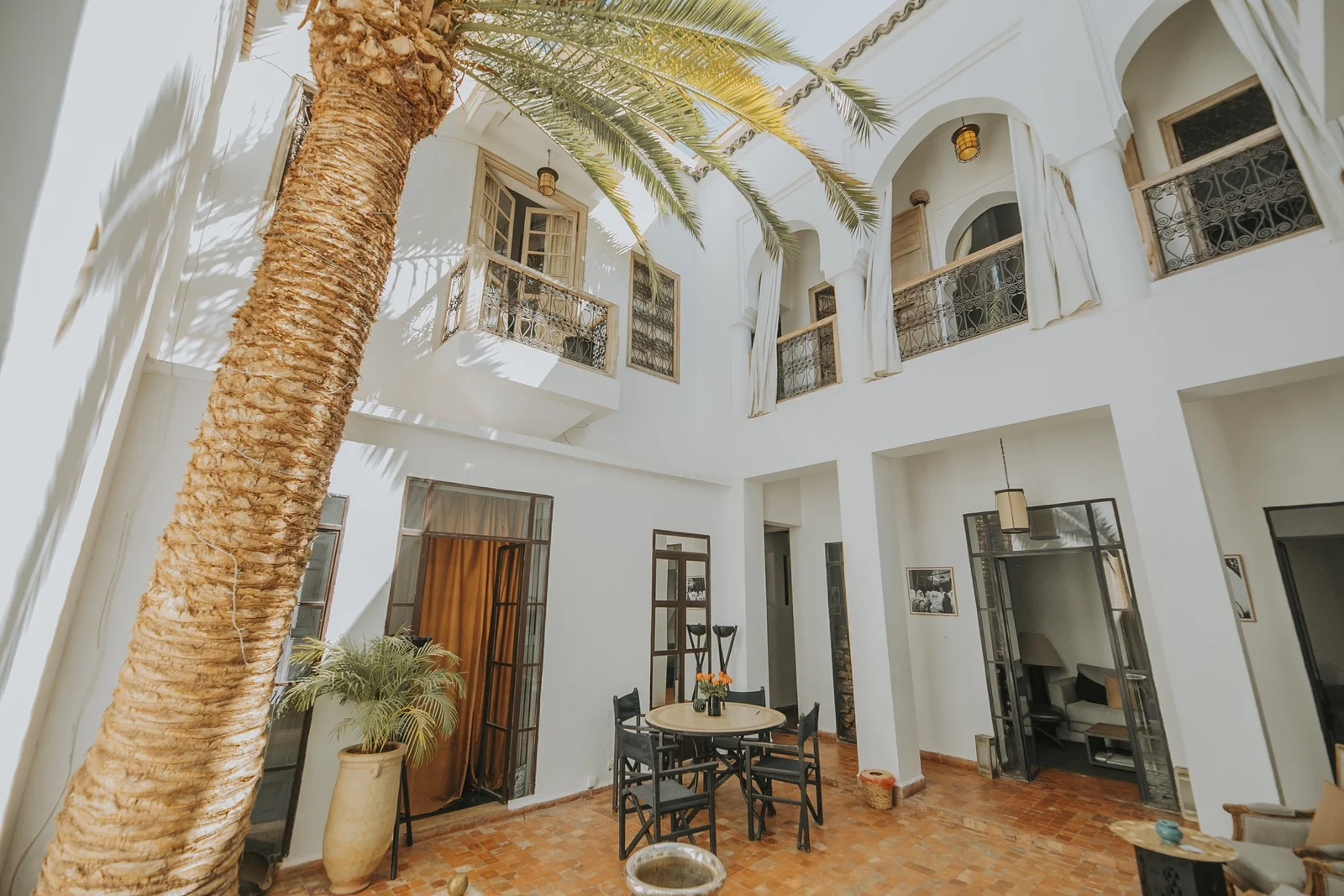 The sunlit patio of Dar Zelda under its palm tree — white arcades, forged-iron balconies and the breakfast table on the terracotta floor