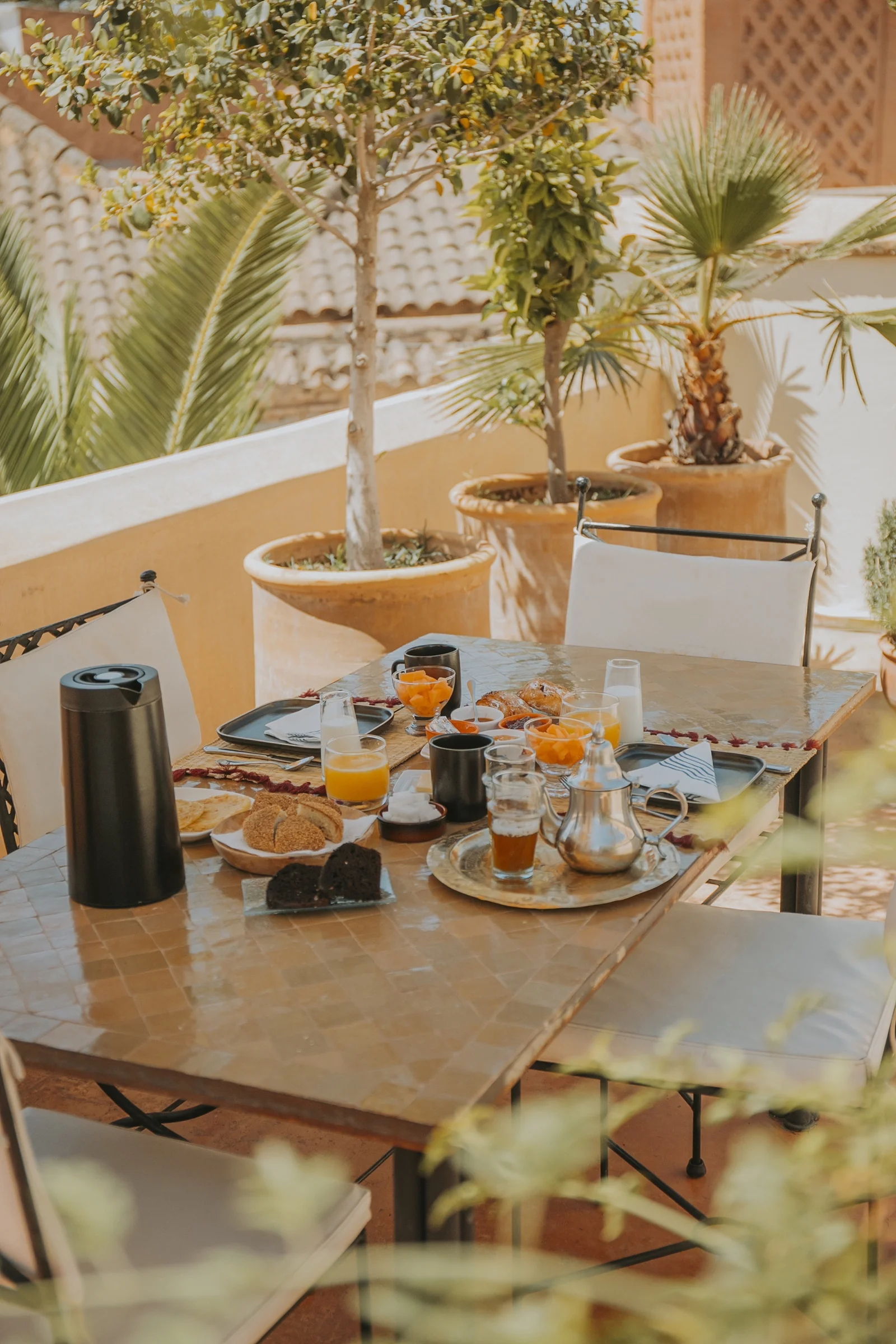 Breakfast on the terrace of Dar Zelda — a brass teapot and fresh orange juice on the zellige table, the medina beyond