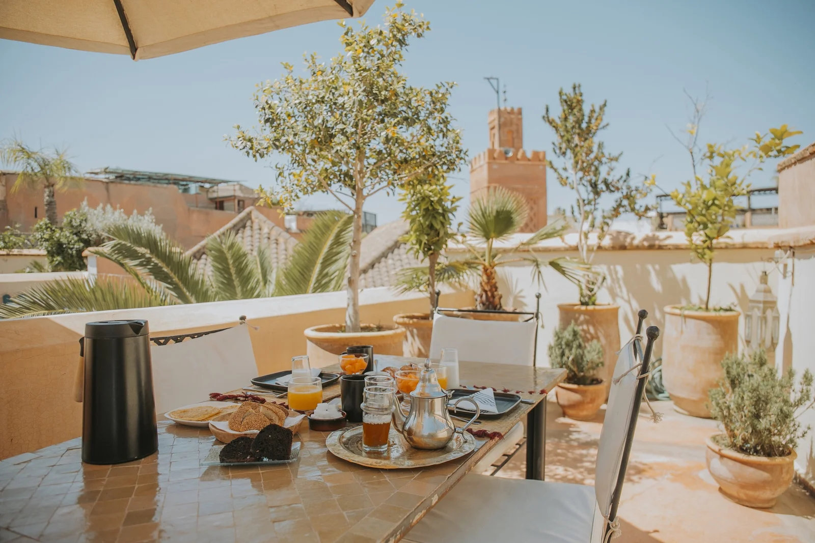 Breakfast on the rooftop of Dar Zelda — silver teapot, pastries and orange juice over the medina roofs