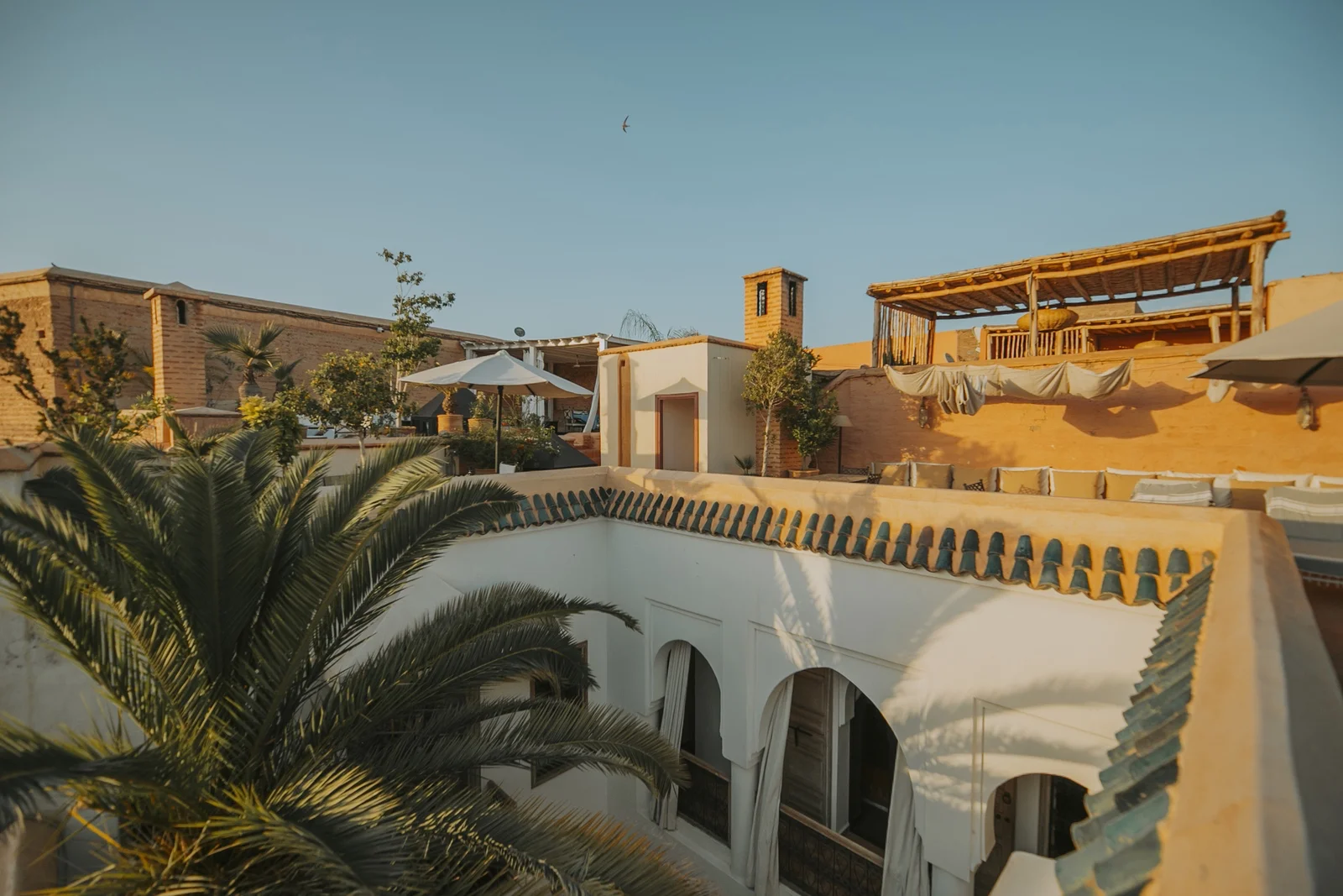 La terrasse sur le toit du Riad Dar Zelda à l'heure dorée — pergolas et salons au-dessus des toits de la médina de Marrakech