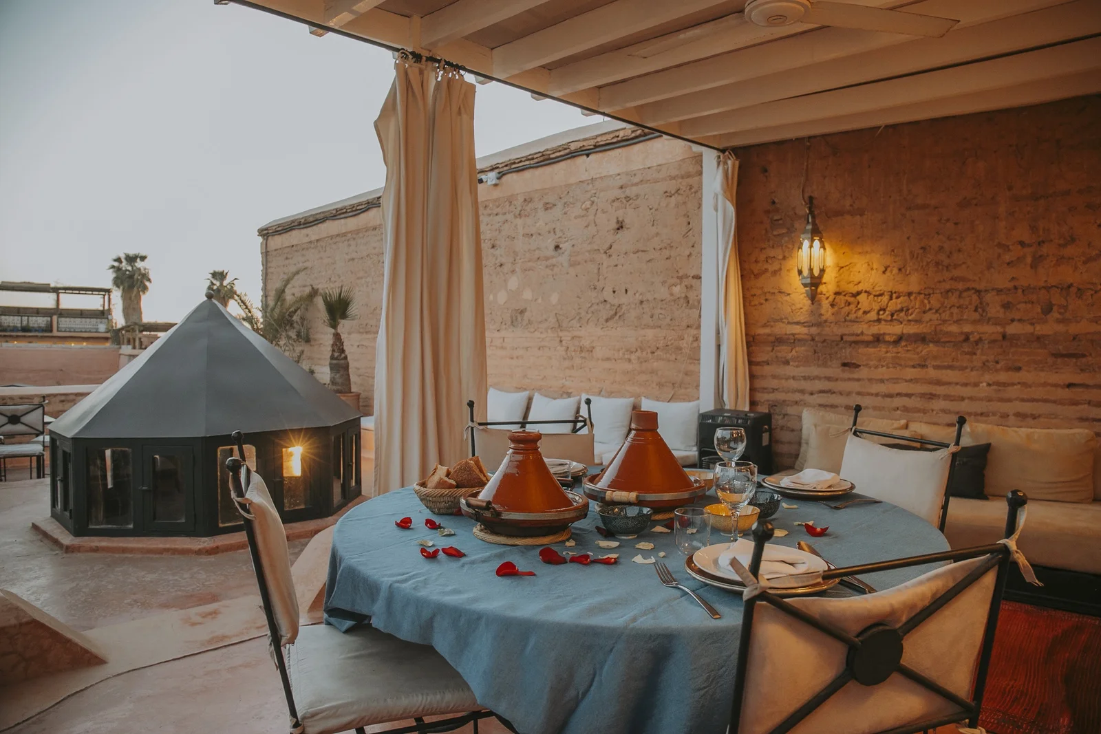 The table d'hôtes set on the rooftop of Dar Zelda at dusk — tagines, rose petals and candlelight under the pergola