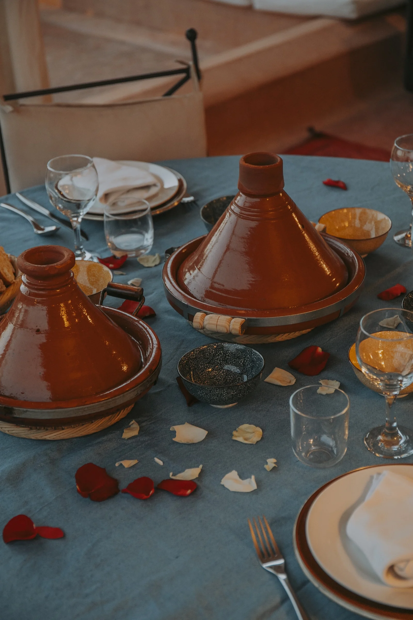 Two glazed tagines on the linen of the table d'hôtes at Dar Zelda, rose petals scattered around